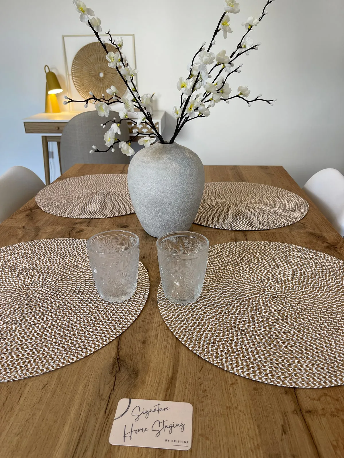 Table en bois dressée avec sets tressés, vase et branches fleuries
